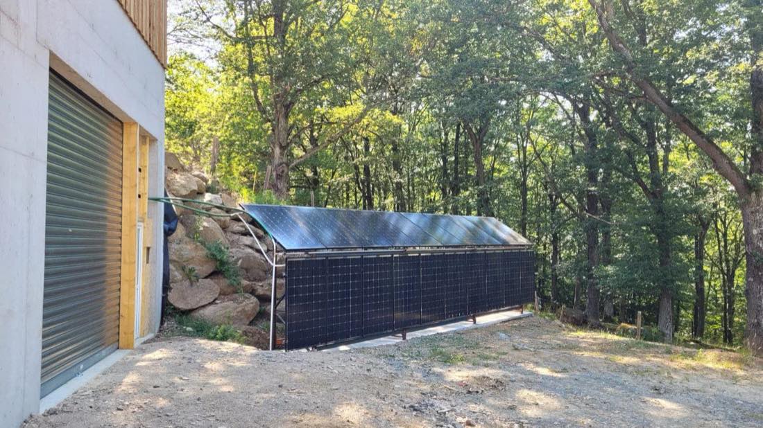 Rangée de capteurs solaires hybrides installés au sol, en lisière de forêt, à côté du bâtiment de séchage